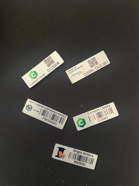 Barcode vs QR code asset tags side by side on a work surface, showing the difference in footprint